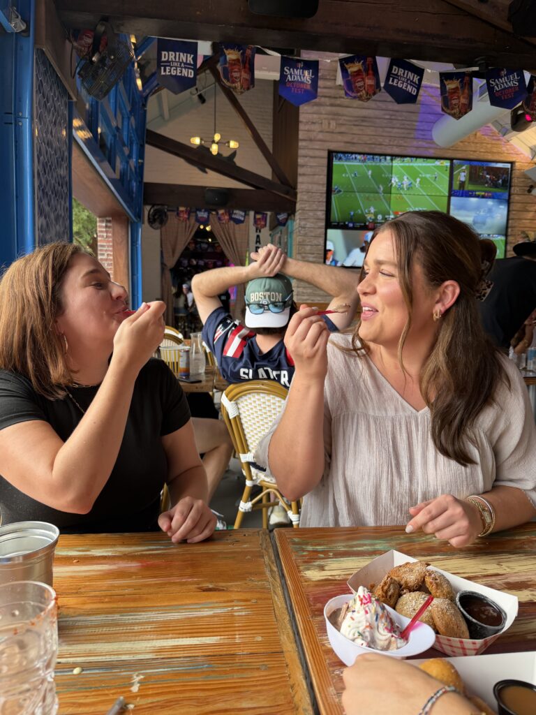 Two women laughing and enjoying desserts and fried food at Share House bar and restaurant in Charleston, SC during a bachelorette party outing planned by Bach Babes