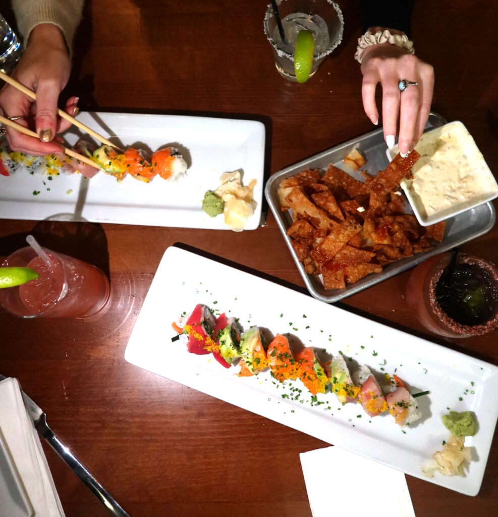 Overhead view of a bachelorette party dinner spread at Mesu in Charleston, SC, featuring colorful sushi rolls, fried appetizers, and margaritas on a wooden table.
