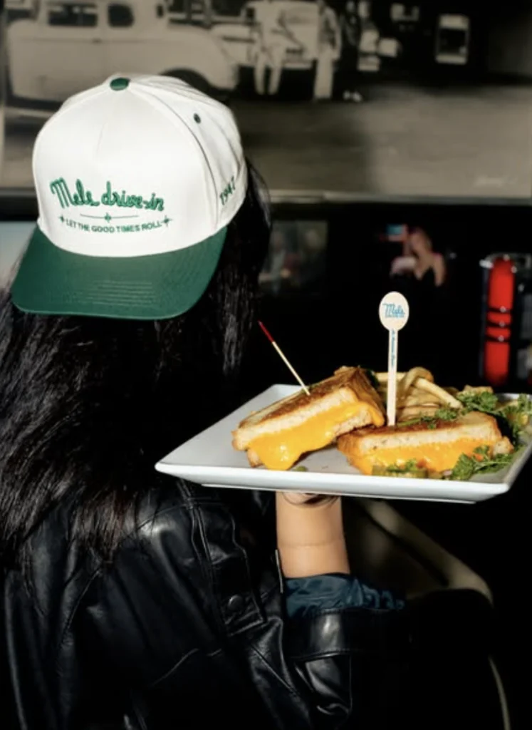 girl wearing a backwards hat holding a tray of grilled cheese from Mels drive in